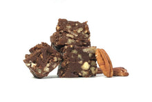 Load image into Gallery viewer, A cross section of our pecan fudge.  There are 3 square chunks about 1&quot; square each and they are stacked stylishly on each other, with one chunk leaning to the left side.  The fudge is full of chopped pecans and a few whole pecans are nearby to show that it&#39;s pecan fudge that we&#39;re showcasing.